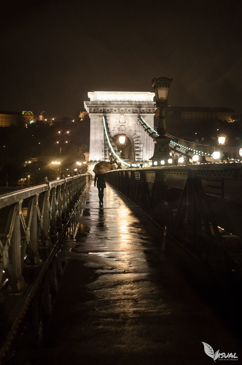 WOMAN WALKING ON ILLUMINATED BRIDGE AT NIGHT