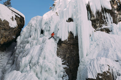 Low angle view of woman climbing on snowcapped mountain during winter