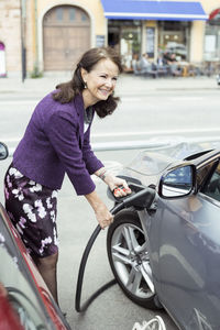 Smiling senior woman refueling car on street