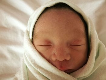 Close-up of baby wrapped in blanket sleeping on bed