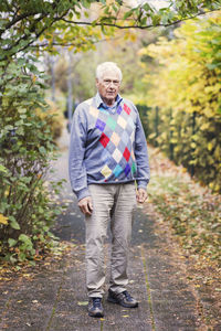 Full length portrait of senior man standing on footpath in park