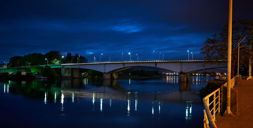 Illuminated bridge over river against sky at night