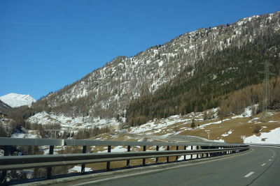 Road by snowcapped mountains against clear blue sky