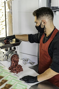 Professional butcher with mask putting meat in mincer machine