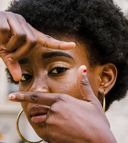 Serious young curly haired african american female making frame with fingers and looking at camera