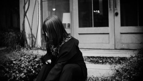 Side view of woman sitting against building