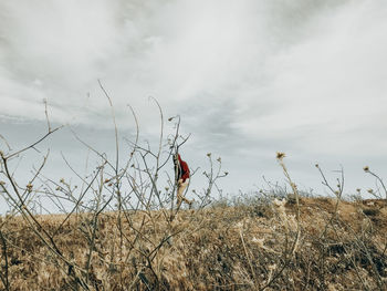 Low angle view of man walking on grassy land against cloudy sky