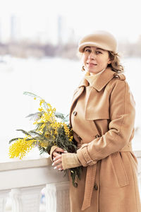 A young woman in a beige coat and hat with a bouquet of mimosa. international women's day