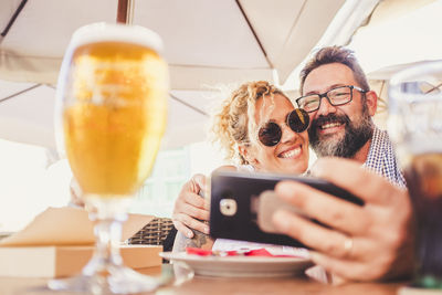 Portrait of smiling couple taking selfie sitting at restaurant