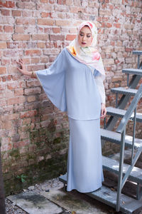 Young woman standing on steps against brick wall