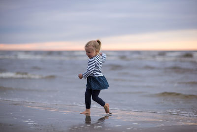 Full length of girl playing at beach against sky during sunset