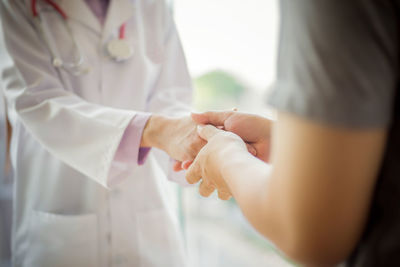 Midsection of female doctor giving handshake at patient