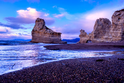 Rock formation on beach against sky during sunset