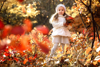 Portrait of cute girl holding autumn leaves standing against plants