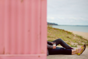 Low section of couple with coffee cup while sitting by wall at beach