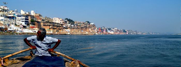 Man sitting on boat in sea against clear sky