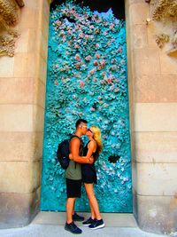 Full length of couple kissing against blue patterned wall at sagrada familia