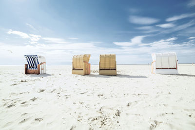 Hooded chairs on beach against sky