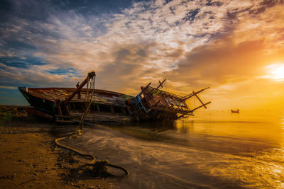 Abandoned boat on shore against sky during sunset