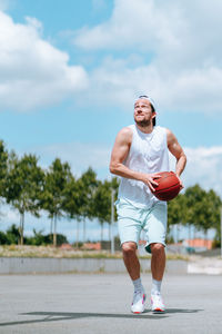 Mid adult man playing with basketball against sky