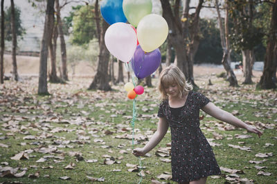 Young woman holding balloons while standing on field