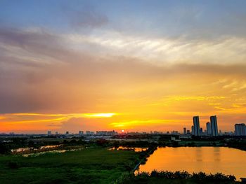 Scenic view of river by buildings against sky during sunset