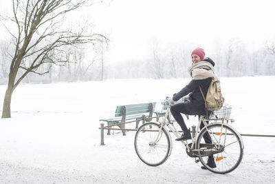 Side view portrait of smiling woman riding bicycle on snow during winter