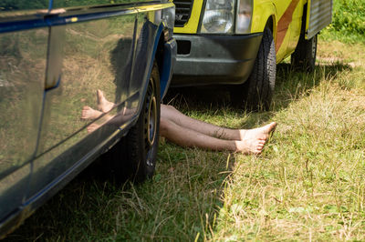 Low section of man relaxing by cars on grassy field
