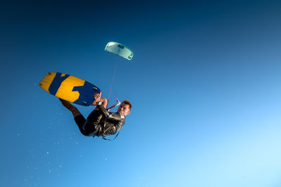 Sports kitesurfer in the air doing a trick with a wakeboard, rider in a wetsuit on a clear blue sky