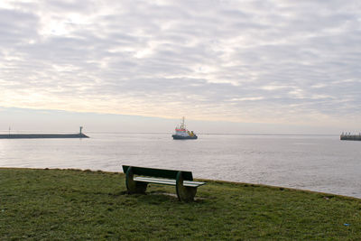 Empty bench on field against seascape