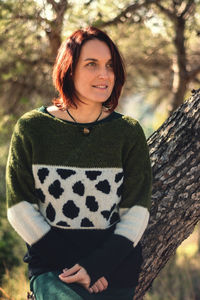 Model with red hair and sweater supported by a tree