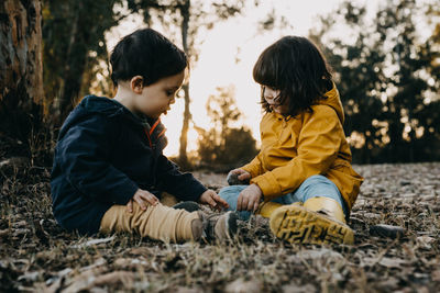 Cute sibling sitting on leaves at park