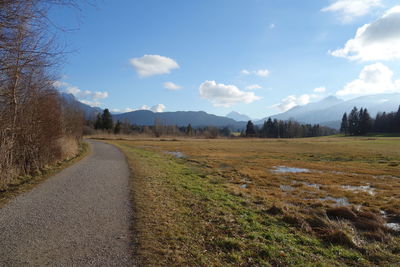 Hiking trail amids fields against sky