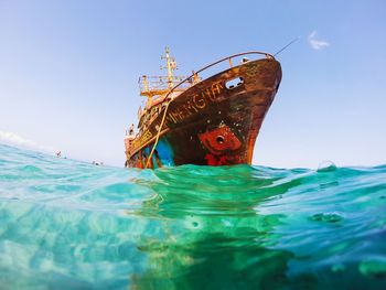 Low angle view of abandoned boat in sea against clear blue sky