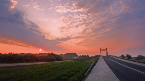 Road amidst field against sky during sunset