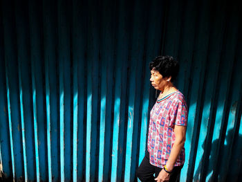 Young man looking away while standing against blue wall