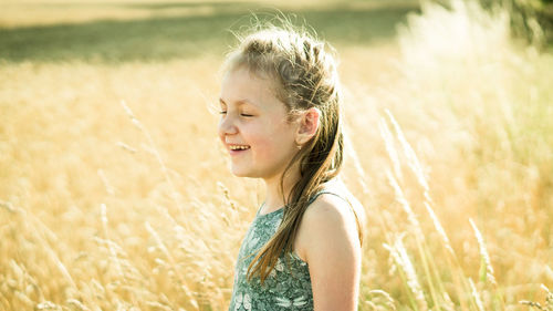 Side view of smiling girl standing on field during sunny day