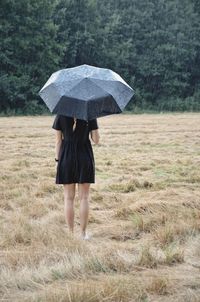 Rear view of woman with umbrella standing on field in the rain