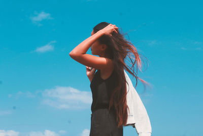 Low angle view of woman standing against blue sky