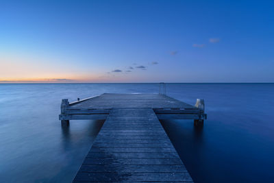 Pier on sea against clear sky at sunset