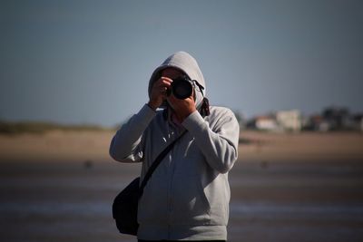 Man photographing with camera at beach against sky