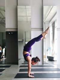 Side view full length of young woman exercising on mat at gym