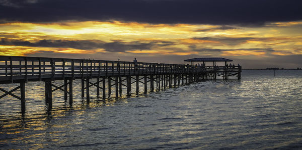 Pier over sea against cloudy sky during sunset