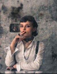 Portrait of young woman smoking against wall