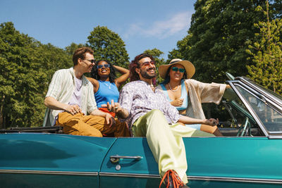 Happy fashionable male and female friends enjoying while sitting in vintage car at sunny day