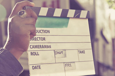 Cropped hand of man holding film slate while standing outdoors