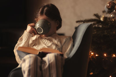 Girl drinking coffee while reading book in darkroom