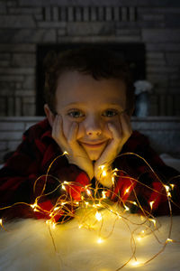 Portrait of boy sitting by illuminated lighting equipment