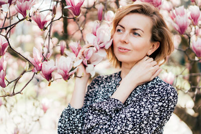 Portrait of woman with pink flowers against tree