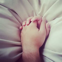 Cropped hands of couple on bed at home